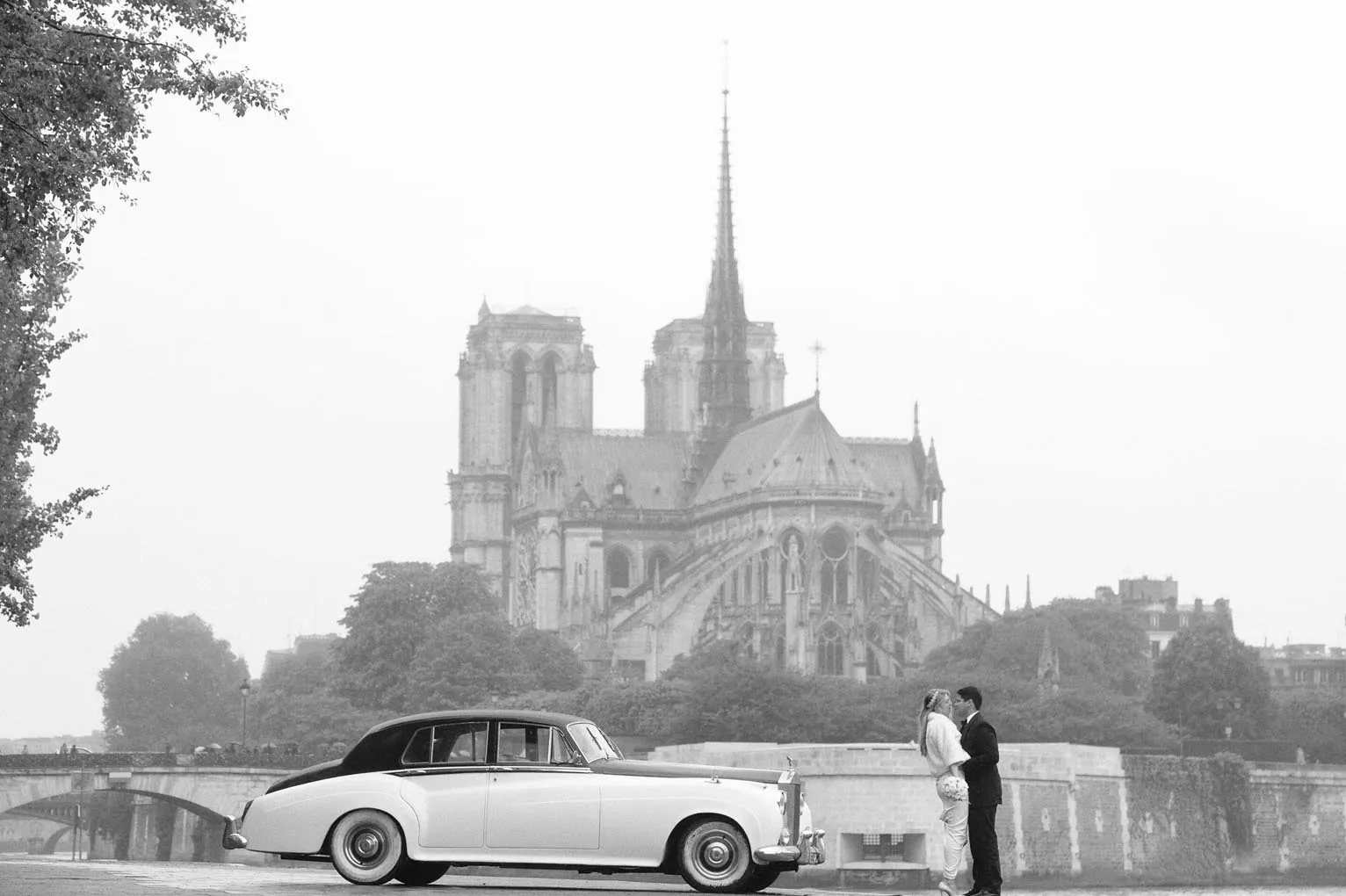 Newlyweds beside a classic car with Notre-Dame in the distance